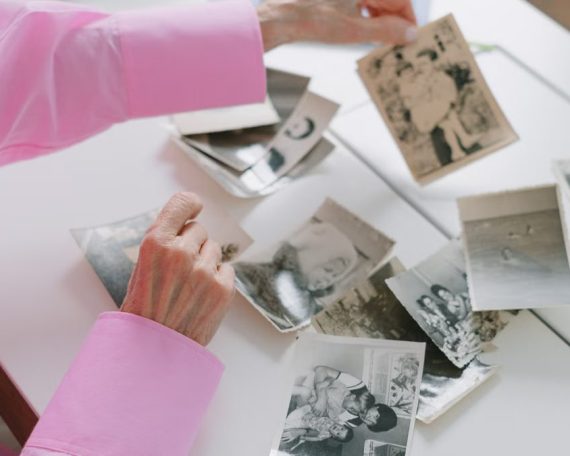 An elderly woman in a pink shirt sorting through old black and white family photographs, evoking nostalgia.