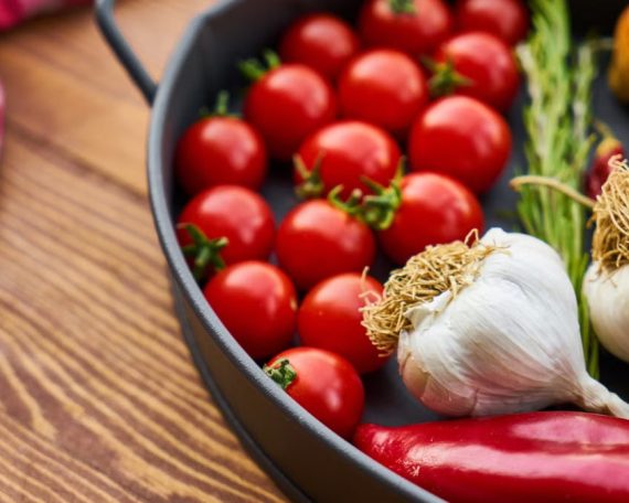 A vivid display of fresh Mediterranean vegetables on a wooden table with a pan.